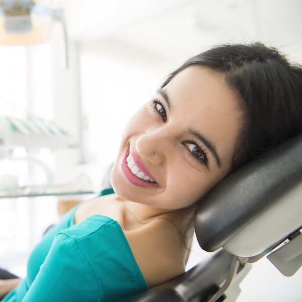Young woman with dark hair in a green top looking back and smiling after restorative dentistry