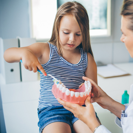 A young girl being shown how to brush teeth as part a family dentistry visit
